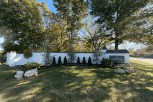 Entrance monument at Forest Ridge neighborhood in Broken Arrow, Oklahoma, with manicured landscaping, evergreen trees, and white brick wall under sunny skies.