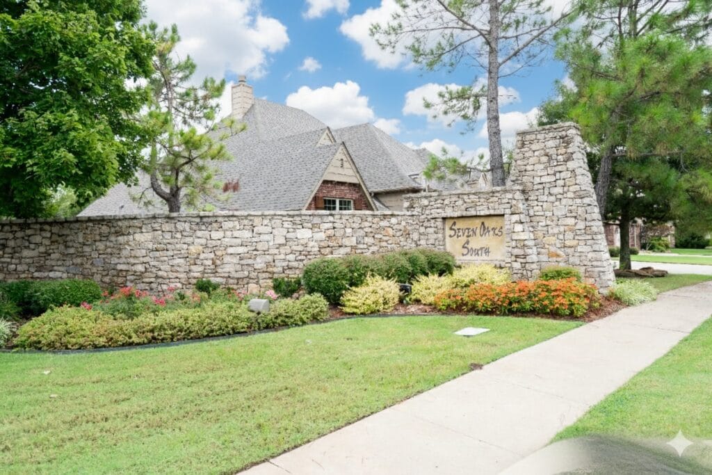 Stone entrance sign for Seven Oaks South neighborhood in Broken Arrow, Oklahoma, surrounded by landscaped greenery and mature trees.