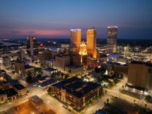 Aerial view of the Tulsa skyline at dusk with city lights and downtown buildings, representing the local market when making offer on house Tulsa.